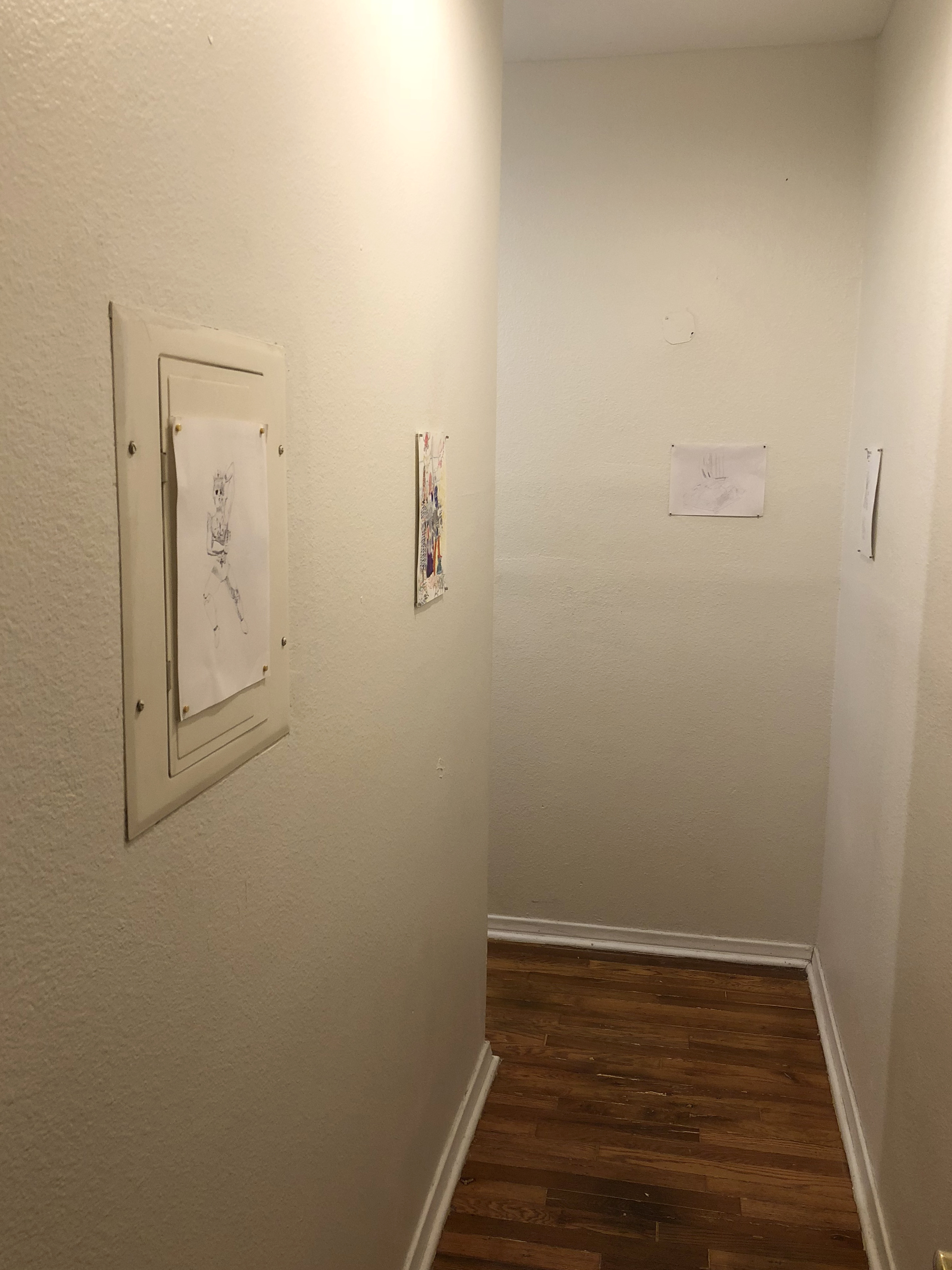 Four drawings on paper hung in a narrow white hallway
